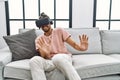 Handsome hispanic man afraid wearing virtual reality glasses at the living room at home