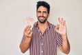 Handsome hispanic man with beard holding united kingdom pounds doing ok sign with fingers, smiling friendly gesturing excellent