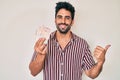 Handsome hispanic man with beard holding united kingdom pounds pointing thumb up to the side smiling happy with open mouth