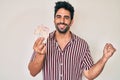 Handsome hispanic man with beard holding united kingdom pounds screaming proud, celebrating victory and success very excited with