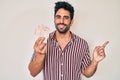 Handsome hispanic man with beard holding united kingdom pounds smiling happy pointing with hand and finger to the side