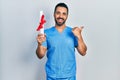 Handsome hispanic man with beard wearing blue male nurse uniform holding diploma pointing thumb up to the side smiling happy with Royalty Free Stock Photo