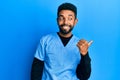 Handsome hispanic man with beard wearing blue male nurse uniform smiling with happy face looking and pointing to the side with Royalty Free Stock Photo