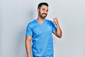 Handsome hispanic man with beard wearing blue male nurse uniform smiling with happy face looking and pointing to the side with Royalty Free Stock Photo