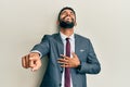 Handsome hispanic man with beard wearing business suit and tie laughing at you, pointing finger to the camera with hand over body, Royalty Free Stock Photo