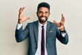 Handsome hispanic man with beard wearing business suit and tie shouting frustrated with rage, hands trying to strangle, yelling Royalty Free Stock Photo