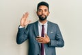 Handsome hispanic man with beard wearing business suit and tie swearing with hand on chest and open palm, making a loyalty promise Royalty Free Stock Photo