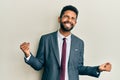 Handsome hispanic man with beard wearing business suit and tie very happy and excited doing winner gesture with arms raised, Royalty Free Stock Photo