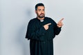 Handsome hispanic man with beard wearing catholic priest robe pointing aside worried and nervous with both hands, concerned and Royalty Free Stock Photo