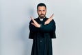 Handsome hispanic man with beard wearing catholic priest robe rejection expression crossing arms doing negative sign, angry face