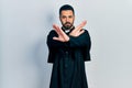 Handsome hispanic man with beard wearing catholic priest robe rejection expression crossing arms and palms doing negative sign,