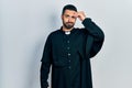 Handsome hispanic man with beard wearing catholic priest robe worried and stressed about a problem with hand on forehead, nervous