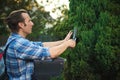 Competent gardener landscaper in gardening uniform, cutting bushes trimming shrubs, tending plants and trees on the yard
