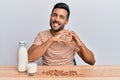 Handsome hispanic man drinking healthy almond milk smiling in love doing heart symbol shape with hands