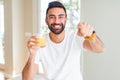 Handsome hispanic man drinking healthy orange juice pointing with finger to the camera and to you, hand sign, positive and Royalty Free Stock Photo