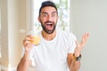 Handsome hispanic man drinking healthy orange juice very happy and excited, winner expression celebrating victory screaming with Royalty Free Stock Photo