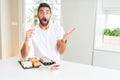 Handsome hispanic man eating asian sushi using chopsticks very happy and excited, winner expression celebrating victory screaming Royalty Free Stock Photo