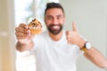 Handsome hispanic man eating chocolate chips muffin happy with big smile doing ok sign, thumb up with fingers, excellent sign Royalty Free Stock Photo