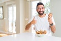 Handsome hispanic man eating chocolate chips muffin happy with big smile doing ok sign, thumb up with fingers, excellent sign Royalty Free Stock Photo