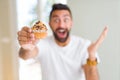 Handsome hispanic man eating chocolate chips muffin very happy and excited, winner expression celebrating victory screaming with Royalty Free Stock Photo