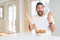 Handsome hispanic man eating chocolate chips muffin very happy and excited, winner expression celebrating victory screaming with Royalty Free Stock Photo