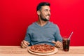 Handsome hispanic man eating tasty pepperoni pizza looking to side, relax profile pose with natural face and confident smile