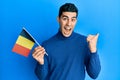 Handsome hispanic man holding belgium flag pointing thumb up to the side smiling happy with open mouth Royalty Free Stock Photo