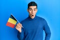 Handsome hispanic man holding belgium flag scared and amazed with open mouth for surprise, disbelief face Royalty Free Stock Photo