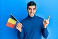 Handsome hispanic man holding belgium flag smiling happy pointing with hand and finger to the side Royalty Free Stock Photo