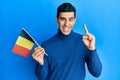 Handsome hispanic man holding belgium flag smiling with an idea or question pointing finger with happy face, number one Royalty Free Stock Photo