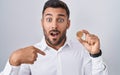 Handsome hispanic man holding cardano cryptocurrency coin pointing finger to one self smiling happy and proud