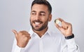 Handsome hispanic man holding cardano cryptocurrency coin pointing thumb up to the side smiling happy with open mouth