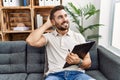 Handsome hispanic man holding clipboard working at psychology clinic smiling confident touching hair with hand up gesture, posing Royalty Free Stock Photo