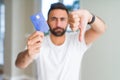 Handsome hispanic man holding credit card with angry face, negative sign showing dislike with thumbs down, rejection concept Royalty Free Stock Photo