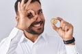 Handsome Hispanic Man Holding Litecoin Cryptocurrency Coin Smiling Happy Doing Ok Sign With Hand On Eye Looking Through Fingers