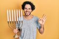 Handsome hispanic man holding menorah hanukkah jewish candle doing ok sign with fingers, smiling friendly gesturing excellent Royalty Free Stock Photo