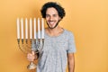 Handsome hispanic man holding menorah hanukkah jewish candle looking positive and happy standing and smiling with a confident Royalty Free Stock Photo
