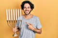 Handsome hispanic man holding menorah hanukkah jewish candle smiling happy pointing with hand and finger Royalty Free Stock Photo