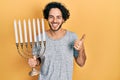 Handsome hispanic man holding menorah hanukkah jewish candle smiling happy and positive, thumb up doing excellent and approval Royalty Free Stock Photo