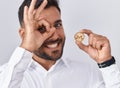 Handsome Hispanic Man Holding Monero Cryptocurrency Coin Smiling Happy Doing Ok Sign With Hand On Eye Looking Through Fingers