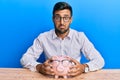 Handsome hispanic man holding piggy bank with glasses depressed and worry for distress, crying angry and afraid Royalty Free Stock Photo