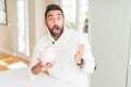 Handsome hispanic man holding piggy bank very happy and excited, winner expression celebrating victory screaming with big smile Royalty Free Stock Photo