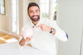 Handsome hispanic man holding piggy bank very happy pointing with hand and finger Royalty Free Stock Photo