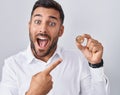 Handsome hispanic man holding polkadot cryptocurrency coin smiling happy pointing with hand and finger