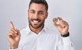 Handsome hispanic man holding polkadot cryptocurrency coin smiling happy pointing with hand and finger to the side
