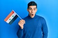 Handsome hispanic man holding syria flag scared and amazed with open mouth for surprise, disbelief face Royalty Free Stock Photo