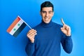 Handsome hispanic man holding syria flag smiling with an idea or question pointing finger with happy face, number one Royalty Free Stock Photo