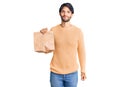 Handsome hispanic man holding take away paper bag thinking attitude and sober expression looking self confident