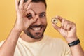 Handsome Hispanic Man Holding Uniswap Cryptocurrency Coin Smiling Happy Doing Ok Sign With Hand On Eye Looking Through Fingers