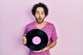 Handsome hispanic man holding vinyl disc afraid and shocked with surprise and amazed expression, fear and excited face